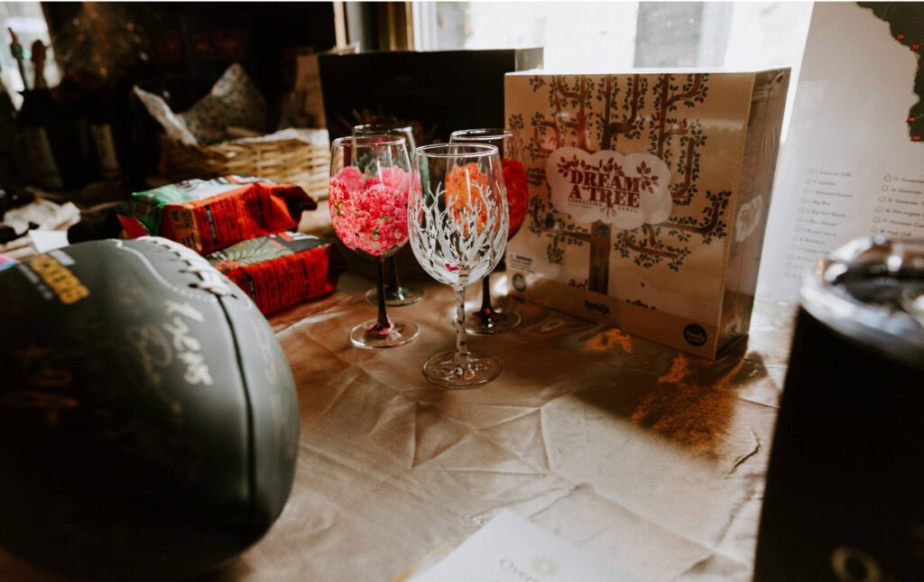 Table display featuring decorated wine glasses, a ‘Dream a Tree’ game, and a signed football at the Madison Waldorf School fundraising auction.